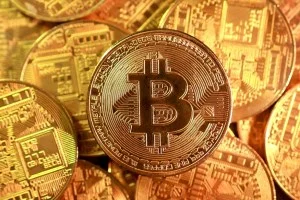 Moeda de Bitcoin dourada em destaque sobre um fundo de gráficos financeiros digitais brilhando em azul e verde, simbolizando alta no mercado.