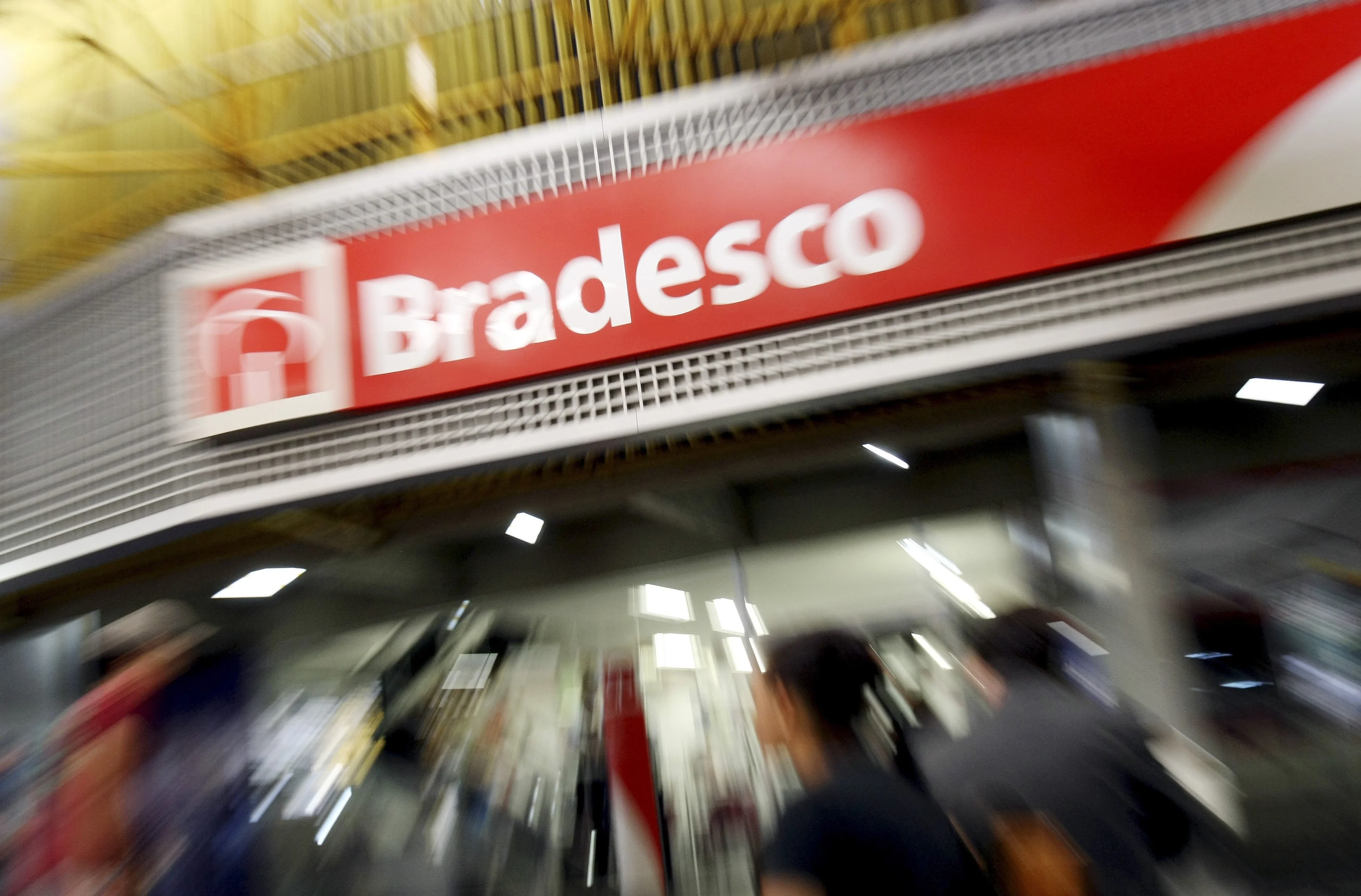 Uma mão segura uma lupa sobre um documento financeiro com gráficos e textos borrados, enquanto ao fundo, um logotipo estilizado de banco aparece em tom sério, refletindo a seriedade das reclamações. A imagem transmite análise e fiscalização financeira.