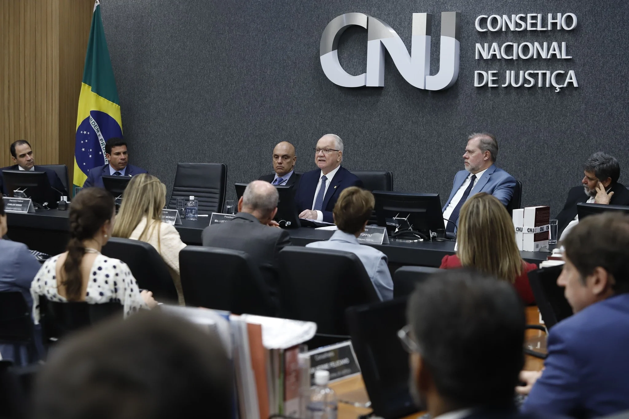 Close-up de um martelo de juiz de madeira sobre uma mesa de tribunal, ao lado de uma calculadora moderna e notas de Real brasileiro, iluminação dramática de estúdio.