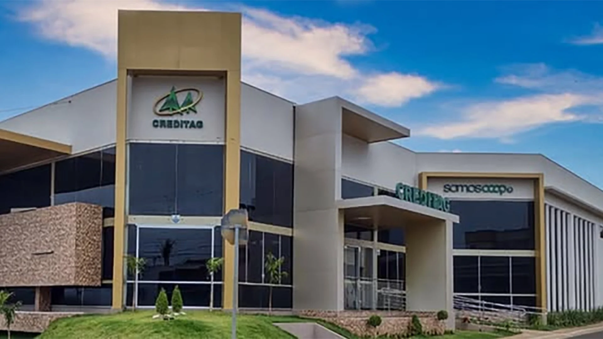 Fachada de um prédio moderno de cooperativa de crédito, com grandes janelas de vidro e o logotipo da Creditag visível na entrada principal, sob um céu claro.