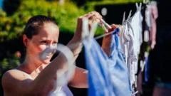 Uma lavanderia moderna e iluminada pelo sol, com uma máquina de lavar de alta tecnologia funcionando. Através da janela, veem-se painéis solares em um jardim.