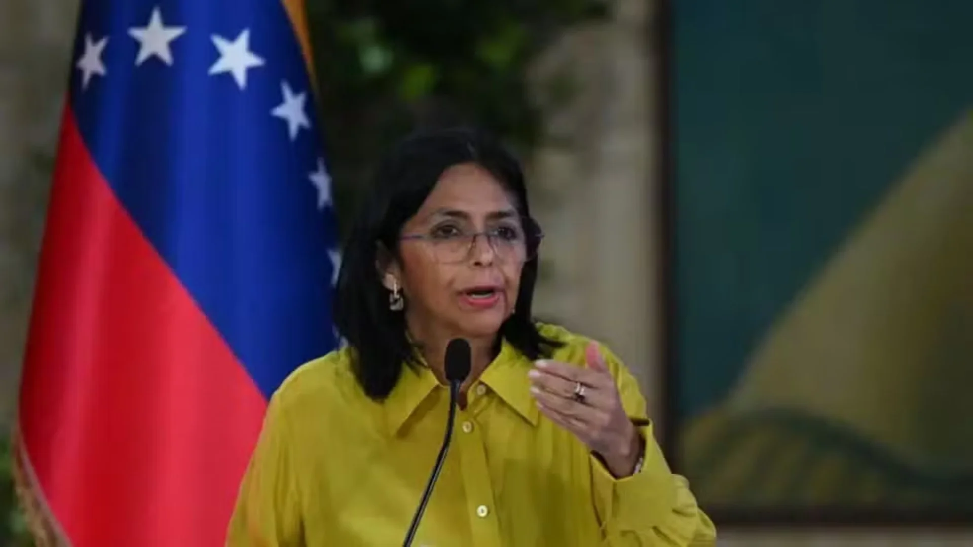 Uma mulher de meia-idade, com cabelos escuros e vestindo blazer, posa para uma foto oficial, representando a presidente interina da Venezuela, Delcy Rodríguez. O fundo é neutro e profissional.