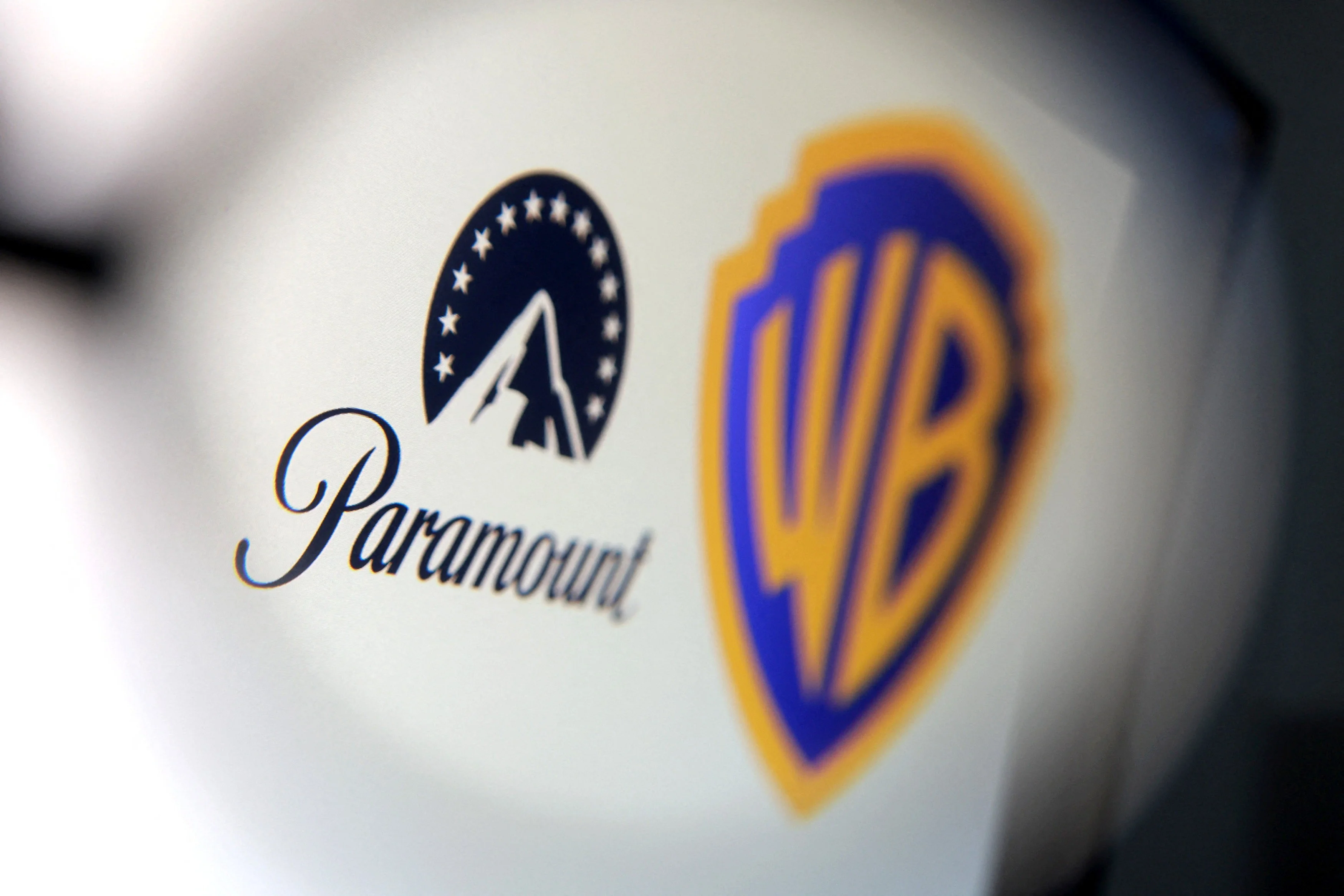 Logotipos da Paramount e Warner Bros. Discovery se unindo, mas interrompidos por um símbolo de decisão judicial, representando o adiamento da fusão bilionária.
