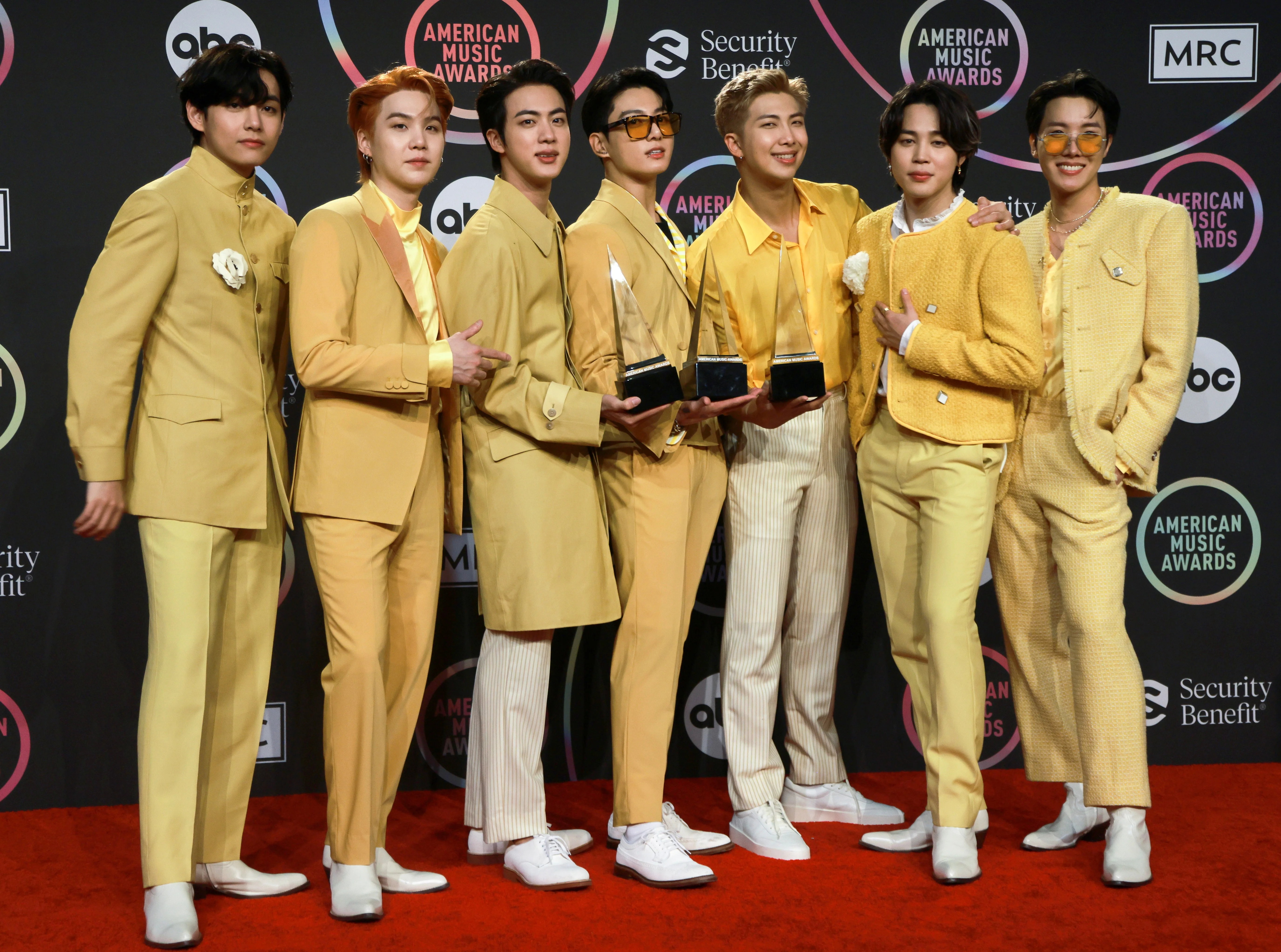 Mão segurando smartphone com site falso de ingressos BTS, imitando Ticketmaster. Cursor aponta para pagamento PIX. Símbolos de dinheiro e cadeado digital ao fundo, representando fraude online.