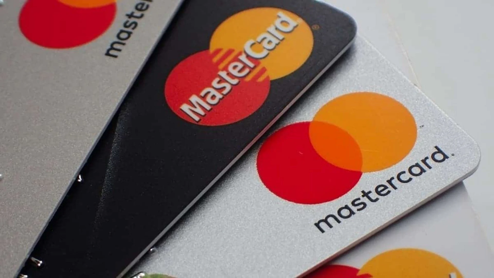 Uma mão segurando um cartão Mastercard digitalizado em um smartphone, com linhas de dados e ícones de outras instituições financeiras interligadas ao fundo, representando a conectividade do Open Finance no Brasil. Cores vibrantes em tons de azul e roxo.