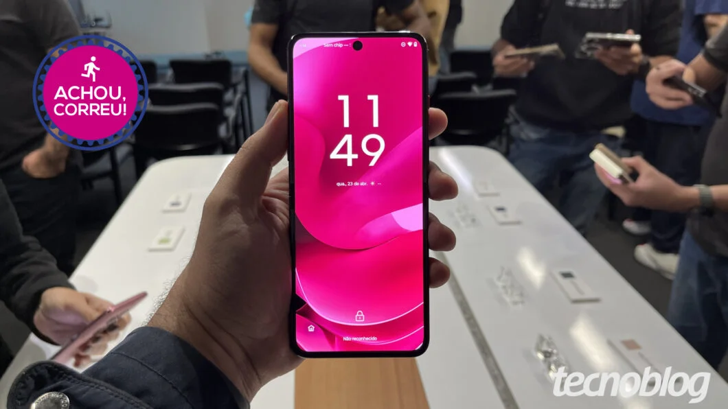 Um smartphone dobrável Motorola Razr 60, na cor preta ou grafite, parcialmente aberto em um ângulo de 45 graus, exibindo a tela interna e a externa, sobre um fundo desfocado que sugere um ambiente de compra online ou uma bancada moderna. Símbolos de desco