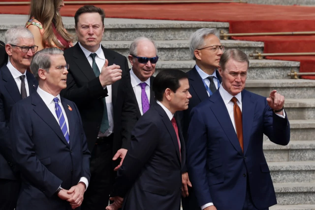 Três proeminentes líderes de empresas de tecnologia (um homem de meia-idade com cabelo escuro e barba, um homem asiático com cabelo curto e óculos, e um homem de meia-idade com cabelo grisalho) sentados à mesa de um jantar formal com um líder político asi