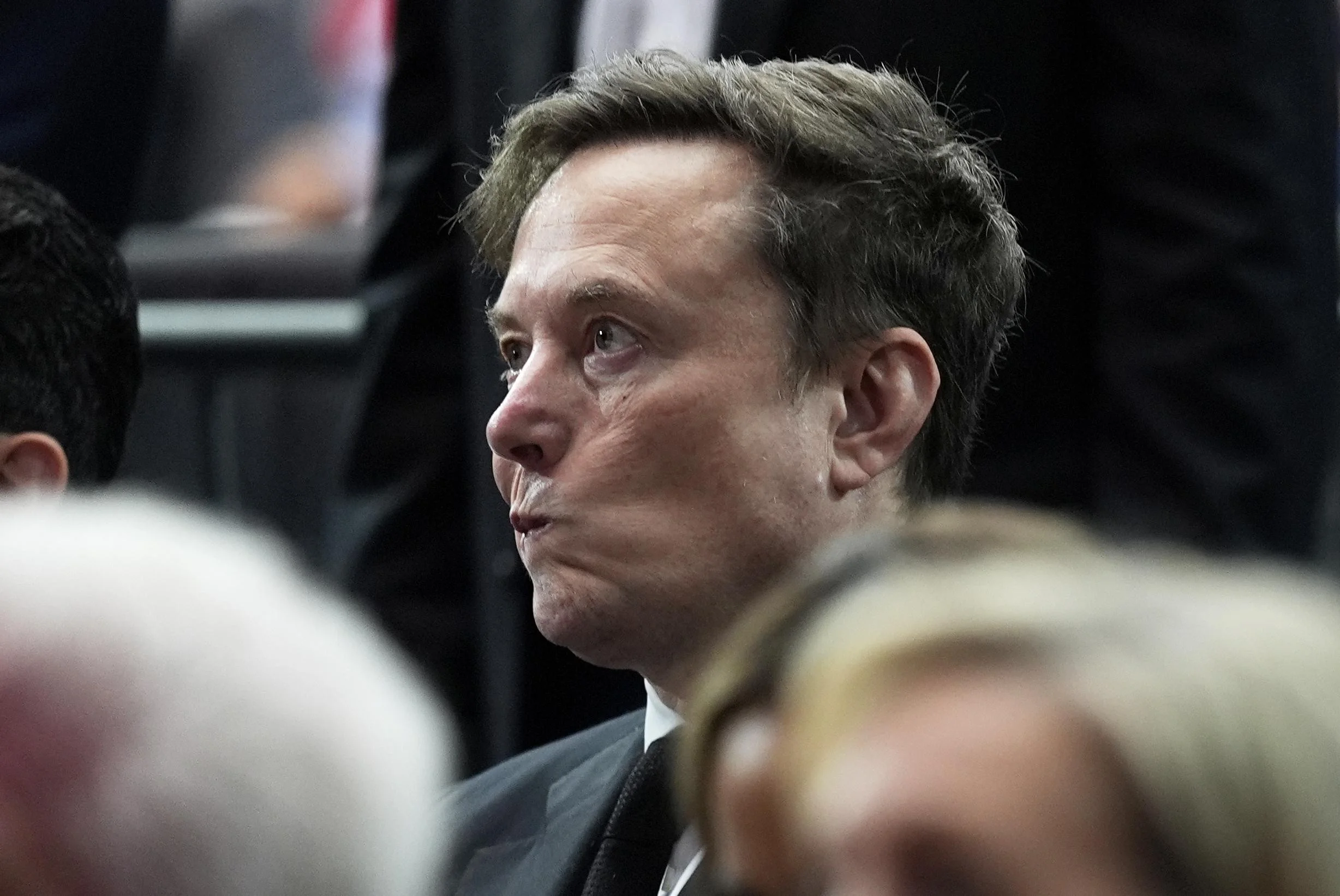 Um gráfico de ações em queda, mostrando setas vermelhas e números negativos sobrepostos a uma silhueta desfocada de um homem que se assemelha a Elon Musk, com logotipos da Tesla e SpaceX ao fundo.