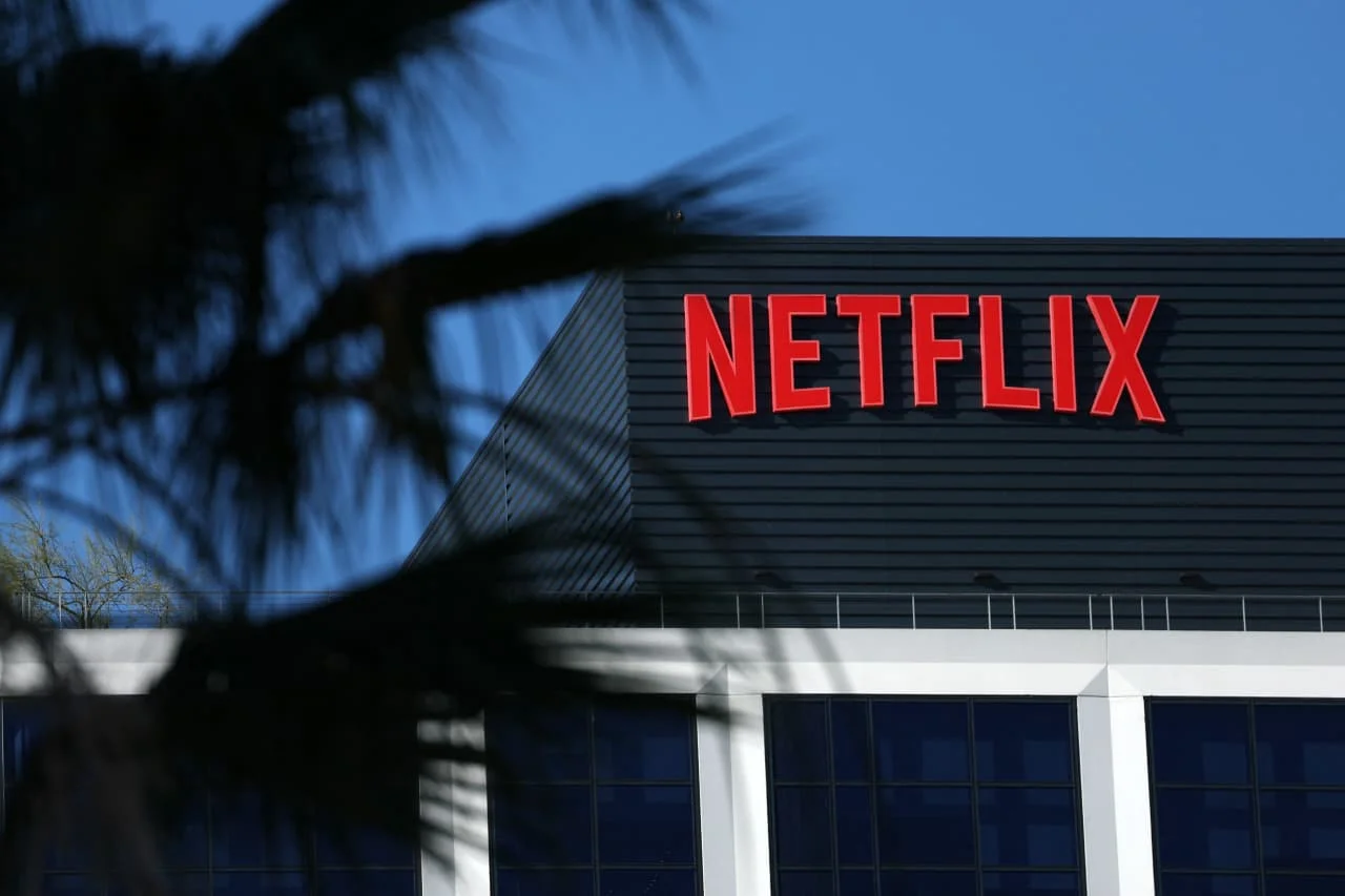 Reed Hastings, co-fundador da Netflix, em um ambiente corporativo moderno. Ele gesticula confiante, com o logotipo da Netflix ao fundo, simbolizando a transição de liderança e a força da empresa no setor de streaming.