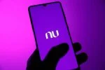Smartphone com interface de aplicativo bancário roxo moderno em destaque, sobre uma mesa de madeira com gráficos financeiros e um cartão de crédito roxo ao lado.