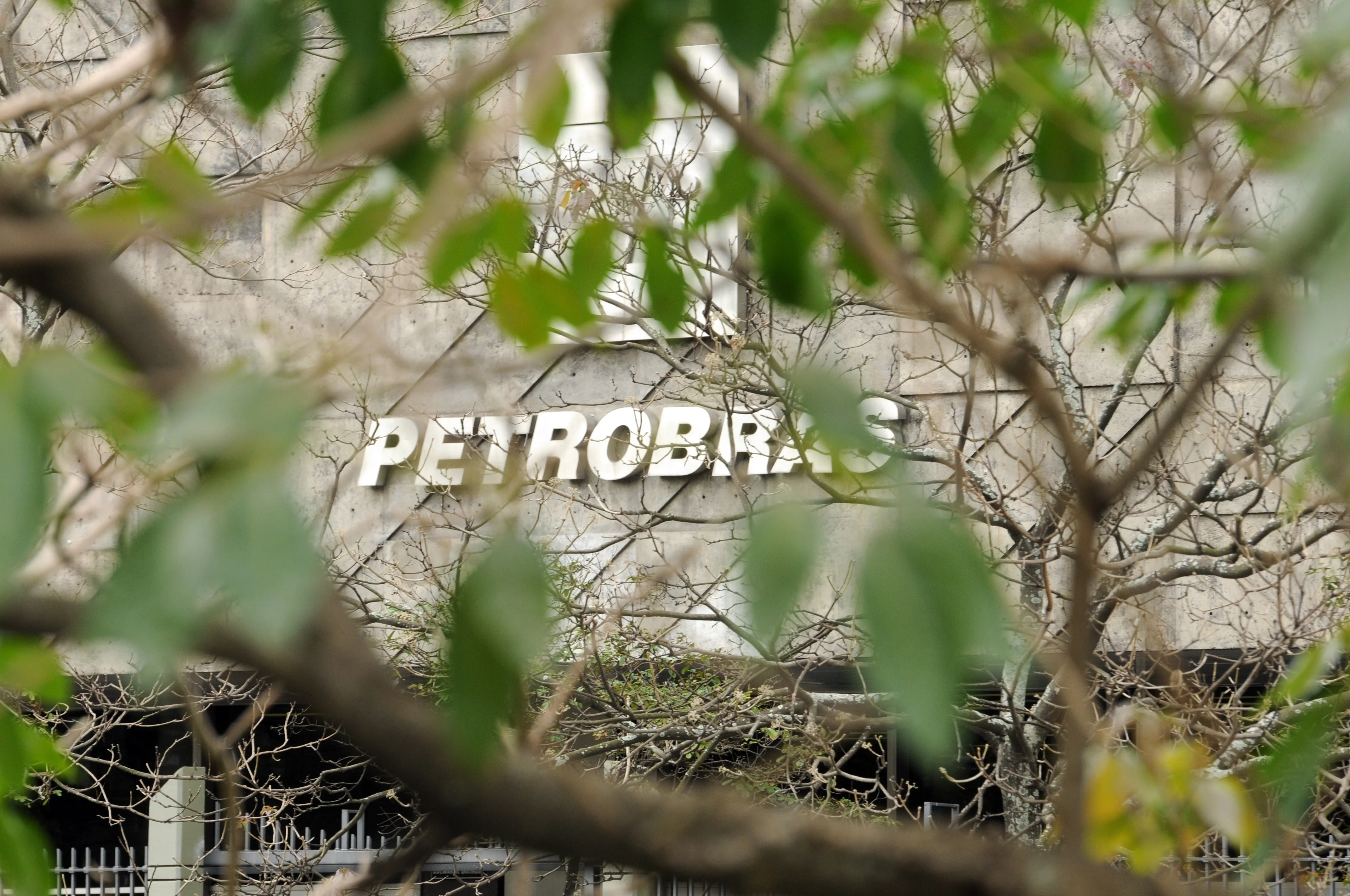 Mãos segurando um punhado de notas de reais, com o logotipo da Petrobras ao fundo, simbolizando a subvenção econômica e o fluxo de dinheiro no setor de energia.
