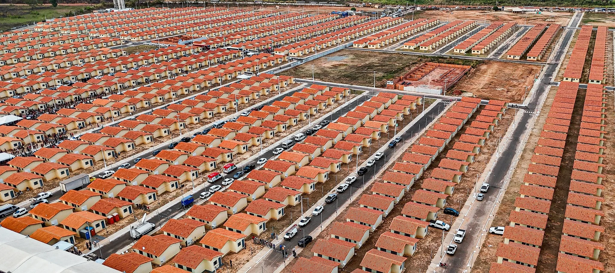 Família brasileira feliz, incluindo um casal e duas crianças, em frente à sua casa recém-reformada, com materiais de construção como tijolos e ferramentas visíveis ao redor, simbolizando a melhoria de moradia.