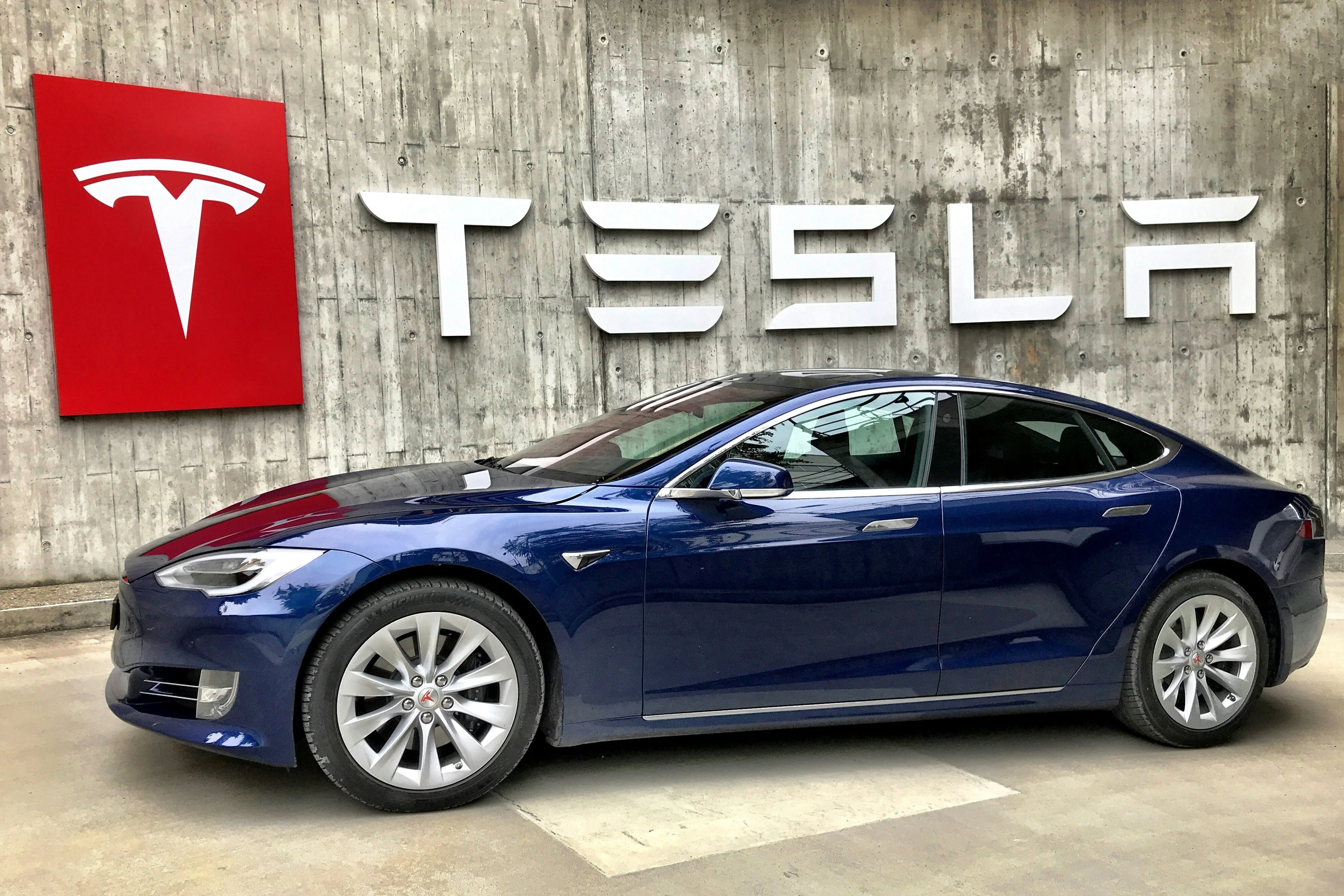 Foguete da SpaceX decolando ao lado de um carro elétrico Tesla em uma estrada futurista, com gráficos de ações em segundo plano e mãos de investidores analisando telas.